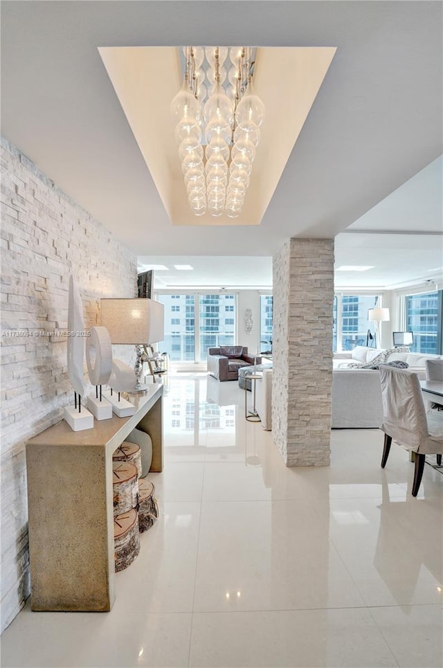 corridor with an inviting chandelier, a tray ceiling, plenty of natural light, and ornate columns