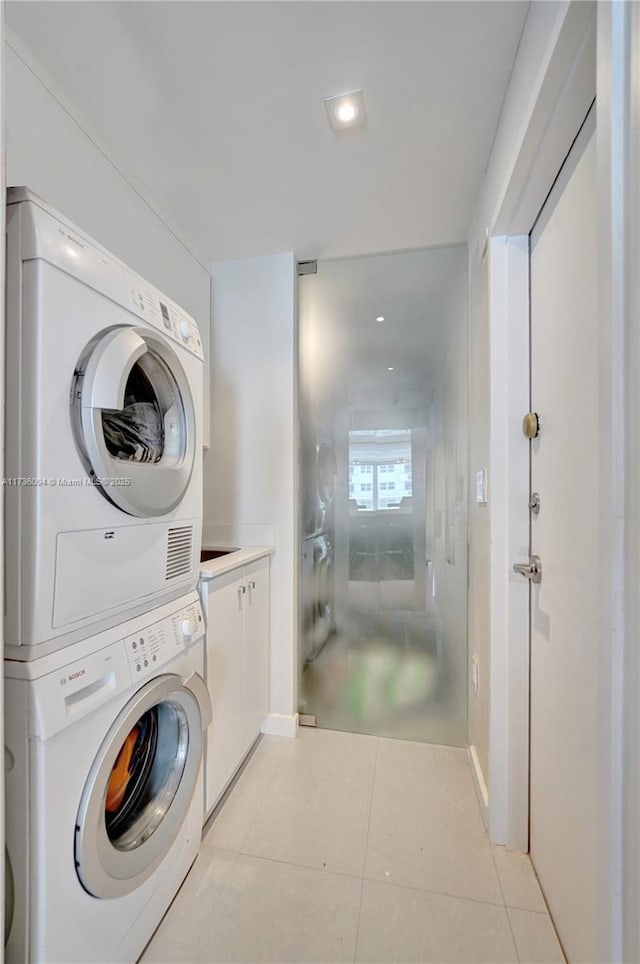 laundry area featuring light tile patterned flooring, cabinets, and stacked washer and clothes dryer