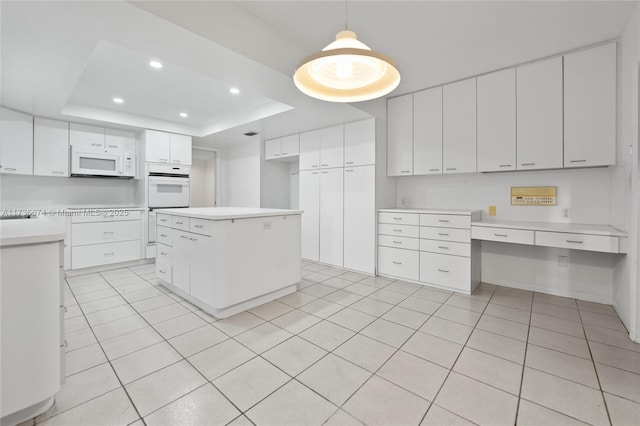 kitchen with white appliances, a tray ceiling, built in desk, white cabinets, and decorative light fixtures