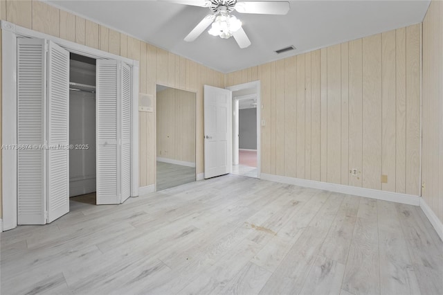 unfurnished bedroom with light hardwood / wood-style floors, a closet, ceiling fan, and wood walls