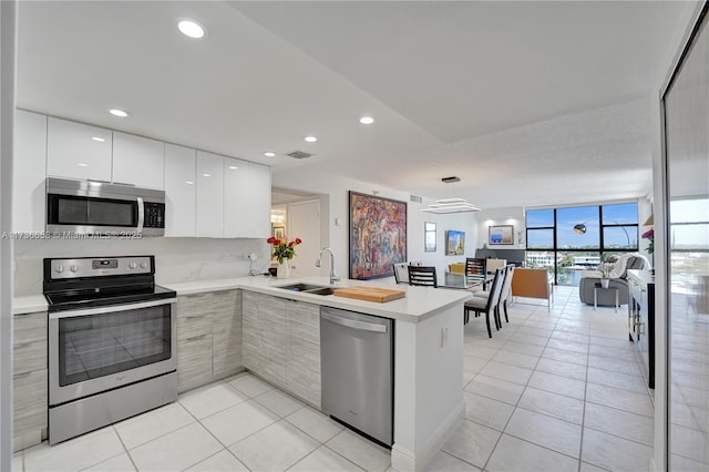 kitchen with white cabinetry, kitchen peninsula, sink, appliances with stainless steel finishes, and light tile patterned flooring