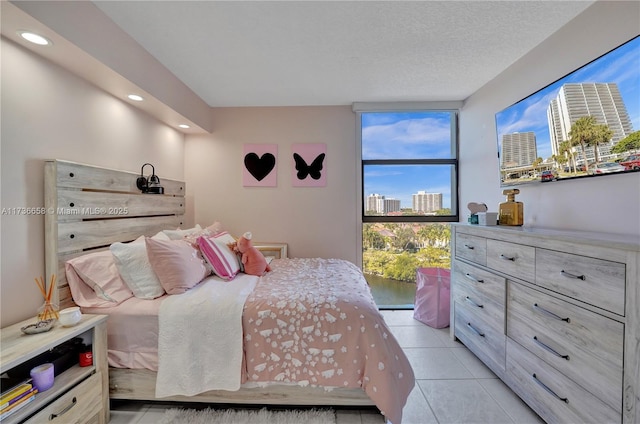 bedroom with a wall of windows, light tile patterned floors, and a textured ceiling