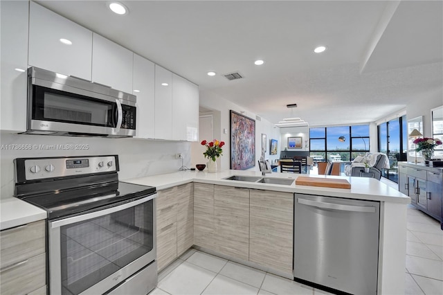 kitchen featuring kitchen peninsula, stainless steel appliances, light tile patterned floors, white cabinets, and light brown cabinets