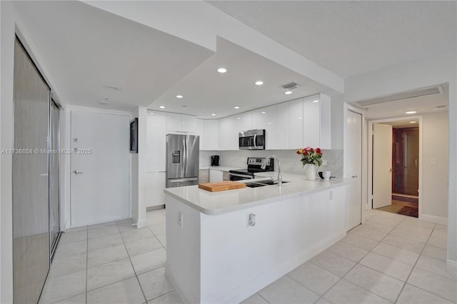kitchen featuring appliances with stainless steel finishes, sink, light tile patterned floors, kitchen peninsula, and white cabinets