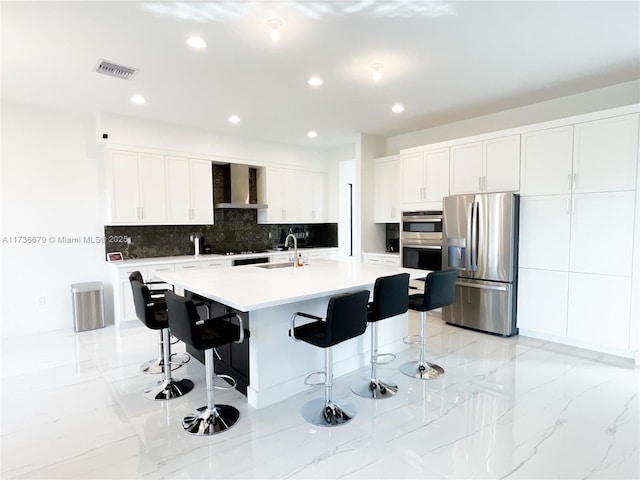 kitchen featuring a breakfast bar, white cabinets, stainless steel refrigerator with ice dispenser, a center island with sink, and wall chimney exhaust hood