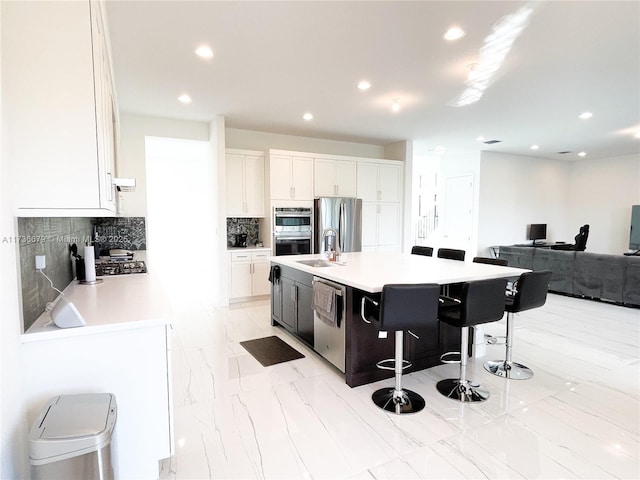 kitchen with a breakfast bar, white cabinetry, tasteful backsplash, a center island with sink, and appliances with stainless steel finishes