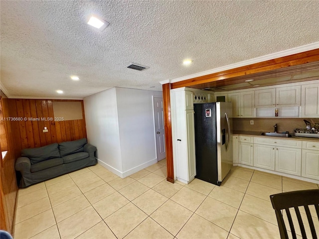 kitchen with light tile patterned flooring, wood walls, sink, stainless steel refrigerator with ice dispenser, and a textured ceiling