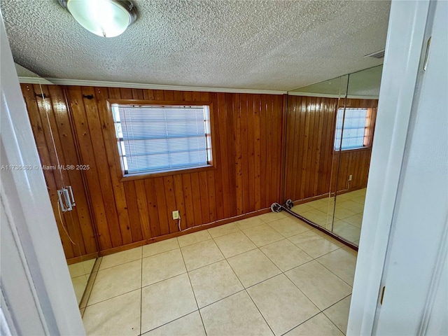 tiled empty room featuring ornamental molding, a textured ceiling, and wood walls