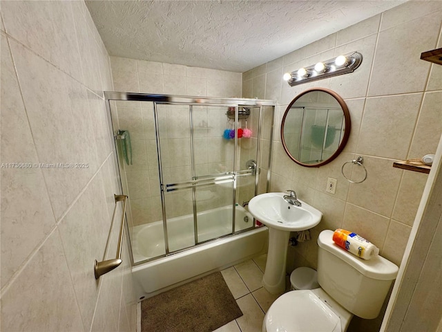 bathroom featuring bath / shower combo with glass door, tile walls, toilet, tile patterned floors, and a textured ceiling