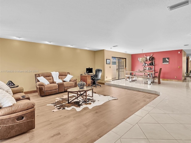 living room featuring a textured ceiling, light wood-type flooring, visible vents, and baseboards