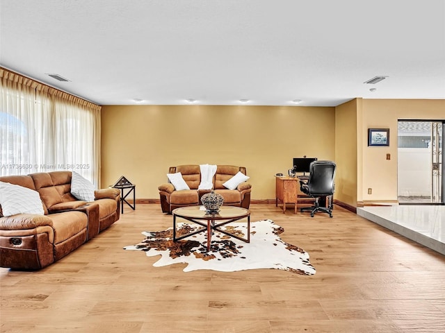 living room featuring light wood finished floors, plenty of natural light, visible vents, and baseboards