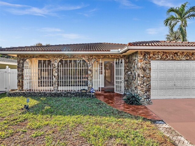 ranch-style home with a tile roof, an attached garage, a front yard, fence, and stone siding