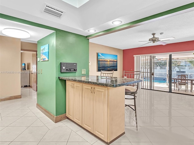 kitchen with visible vents, baseboards, ceiling fan, a breakfast bar, and light tile patterned flooring