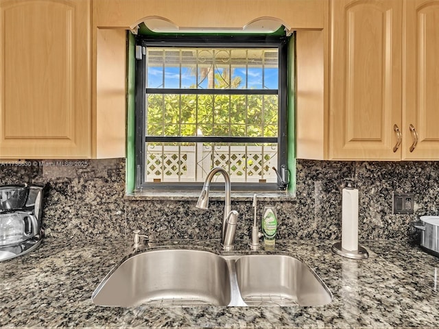 kitchen featuring dark stone counters, light brown cabinets, a sink, and decorative backsplash