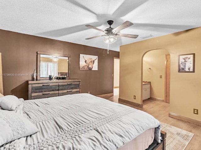 bedroom featuring baseboards, visible vents, arched walkways, a textured ceiling, and light wood-type flooring