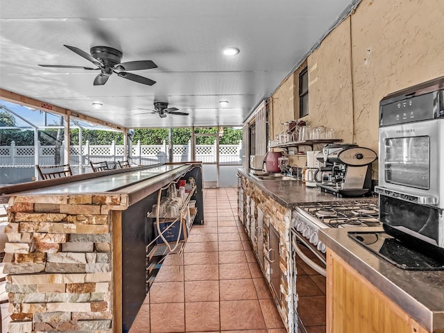 kitchen featuring dark countertops, light tile patterned floors, gas stove, and a sink