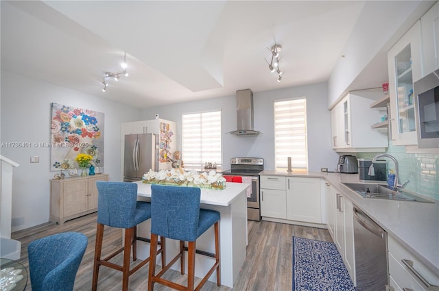 kitchen featuring sink, a breakfast bar, stainless steel appliances, white cabinets, and wall chimney exhaust hood