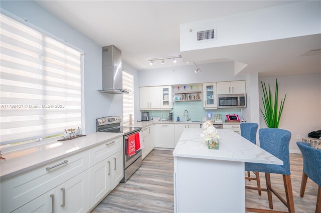 kitchen featuring appliances with stainless steel finishes, a center island, light stone countertops, white cabinets, and wall chimney exhaust hood