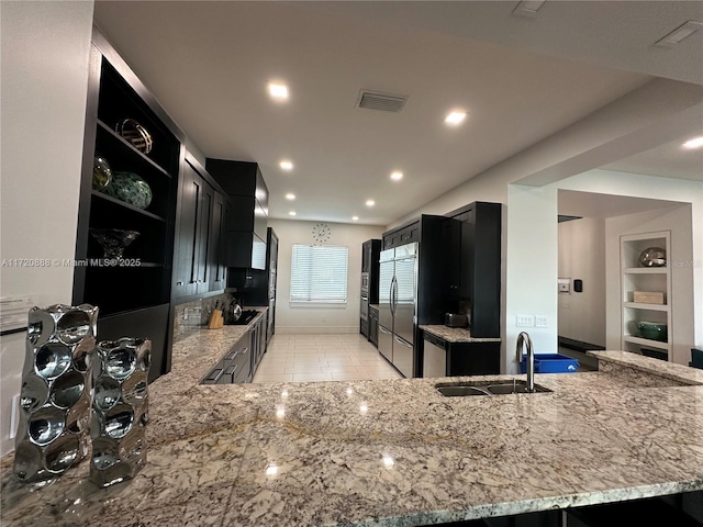 kitchen featuring sink, built in refrigerator, light stone countertops, built in shelves, and kitchen peninsula