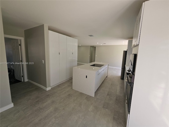 kitchen with hardwood / wood-style floors, white cabinetry, stainless steel fridge, a center island, and black electric stovetop