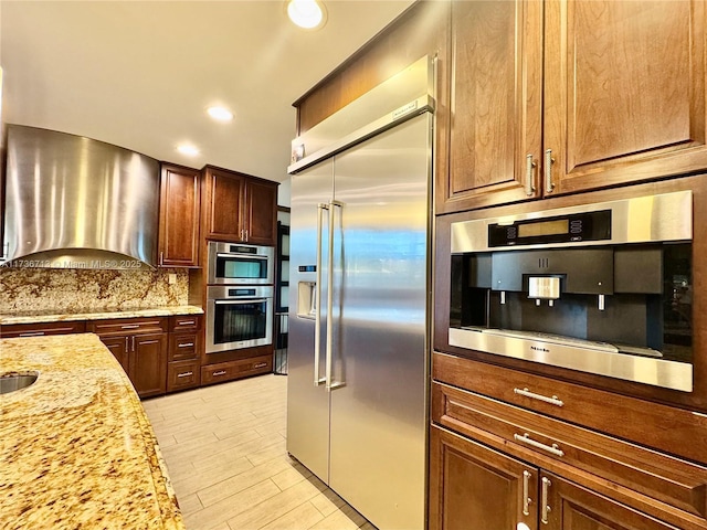 kitchen with decorative backsplash, light stone counters, stainless steel appliances, extractor fan, and recessed lighting