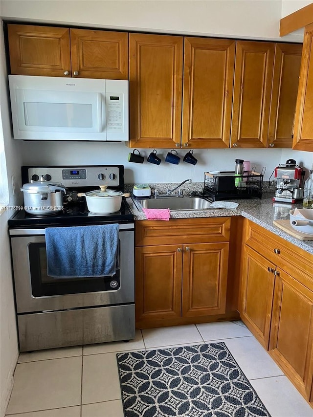 kitchen featuring sink, stone countertops, light tile patterned floors, and stainless steel range with electric cooktop