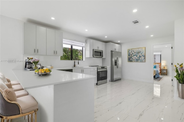 kitchen featuring white cabinetry, sink, a breakfast bar area, kitchen peninsula, and stainless steel appliances