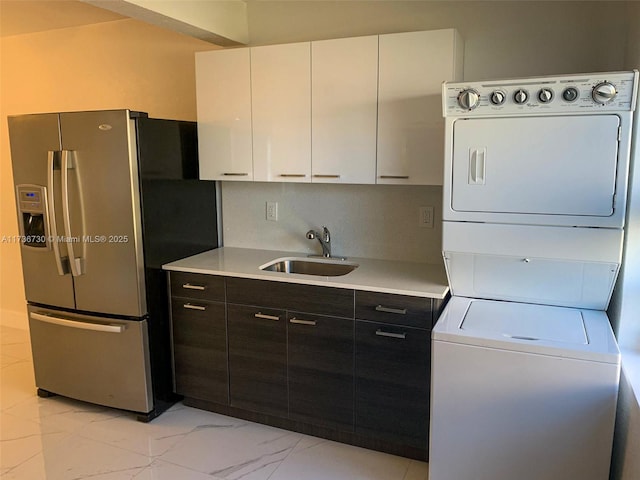 kitchen with stacked washer / dryer, sink, white cabinets, dark brown cabinetry, and stainless steel refrigerator with ice dispenser