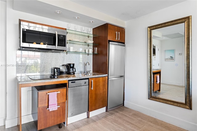 kitchen with appliances with stainless steel finishes, sink, light wood-type flooring, and decorative backsplash