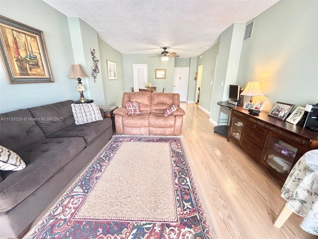 living room featuring ceiling fan, light hardwood / wood-style floors, and a textured ceiling