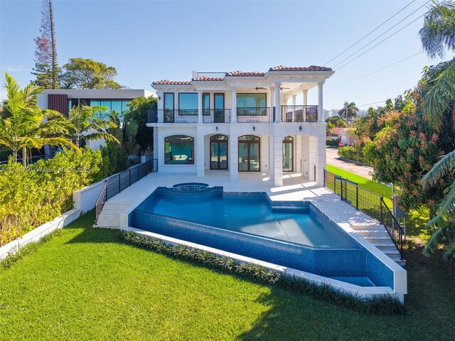 back of property with a balcony, a pool with hot tub, a patio, and a lawn