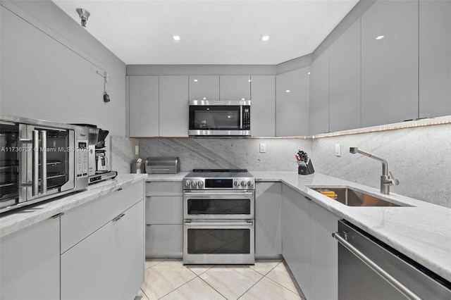 kitchen featuring sink, appliances with stainless steel finishes, gray cabinetry, light stone counters, and tasteful backsplash