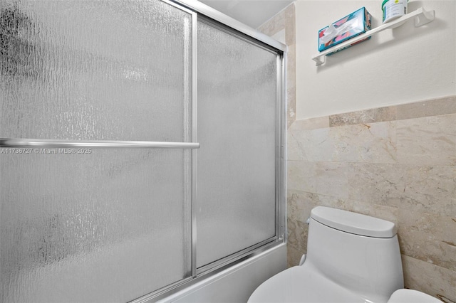 bathroom with bath / shower combo with glass door, tile walls, and toilet