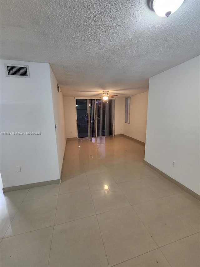 tiled empty room with ceiling fan and a textured ceiling