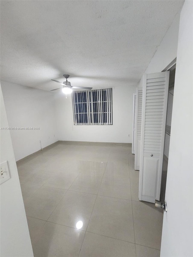 tiled empty room with ceiling fan and a textured ceiling