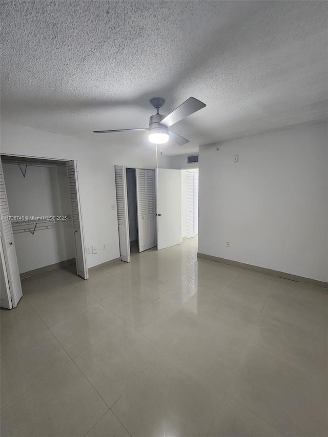 unfurnished bedroom featuring ceiling fan, two closets, and a textured ceiling