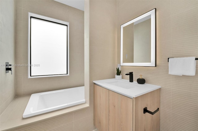 bathroom with tile walls, vanity, and tiled tub