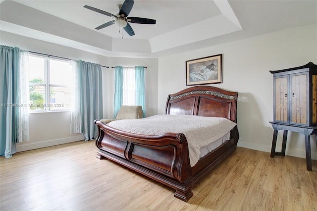 bedroom featuring ceiling fan, a raised ceiling, and light hardwood / wood-style floors