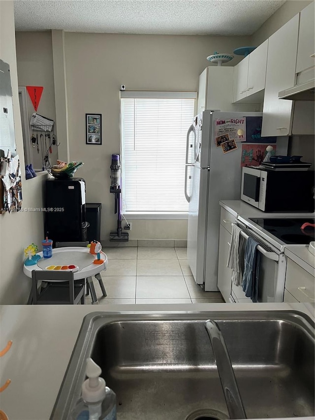 kitchen featuring light tile patterned floors, white appliances, a textured ceiling, and white cabinets