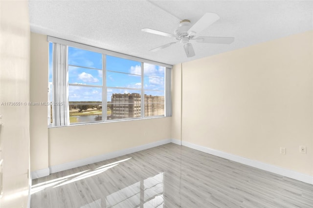 empty room with ceiling fan, a water view, a textured ceiling, and light hardwood / wood-style floors