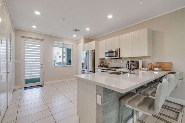 kitchen with appliances with stainless steel finishes, sink, a kitchen bar, decorative backsplash, and kitchen peninsula