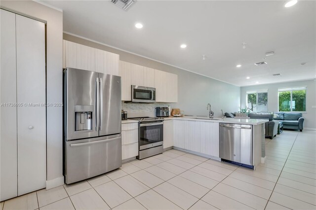 kitchen featuring appliances with stainless steel finishes, sink, decorative backsplash, light tile patterned floors, and kitchen peninsula