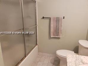 bathroom featuring toilet, bath / shower combo with glass door, and tile patterned flooring