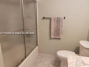 full bath featuring toilet and shower / bath combination with glass door