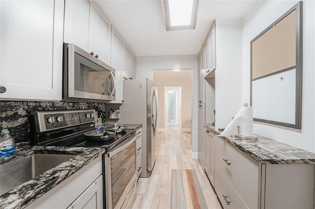 kitchen with light hardwood / wood-style flooring, stainless steel appliances, dark stone counters, and white cabinets