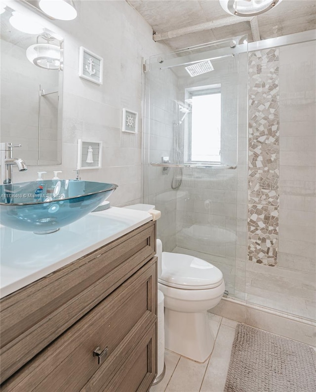 bathroom featuring a shower with door, tile walls, vanity, tile patterned floors, and toilet