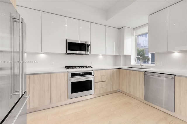 kitchen with stainless steel appliances, light brown cabinetry, light hardwood / wood-style floors, and white cabinets