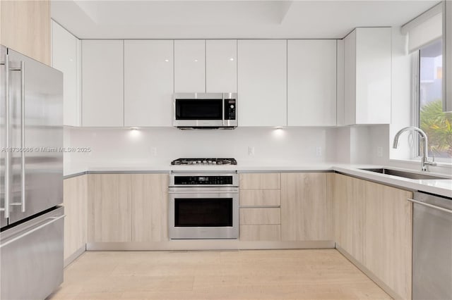 kitchen featuring light brown cabinetry, sink, white cabinetry, stainless steel appliances, and light hardwood / wood-style floors