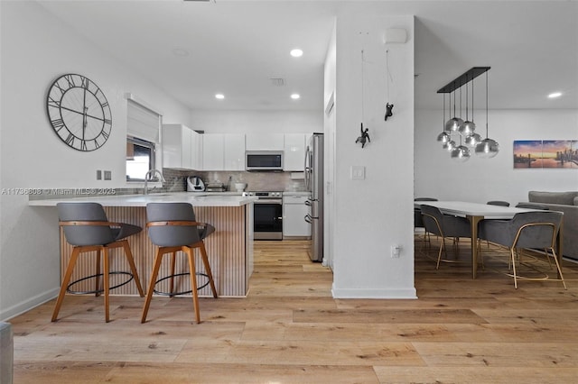 kitchen with appliances with stainless steel finishes, a kitchen breakfast bar, white cabinets, kitchen peninsula, and light wood-type flooring