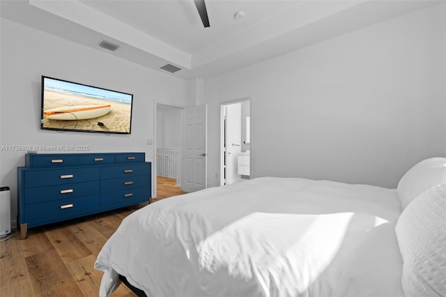 bedroom featuring a raised ceiling, wood-type flooring, ensuite bathroom, and ceiling fan